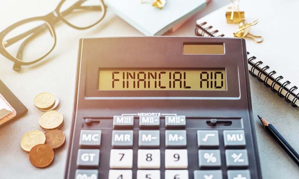 Word FINANCIAL AID written on calculator on office table.