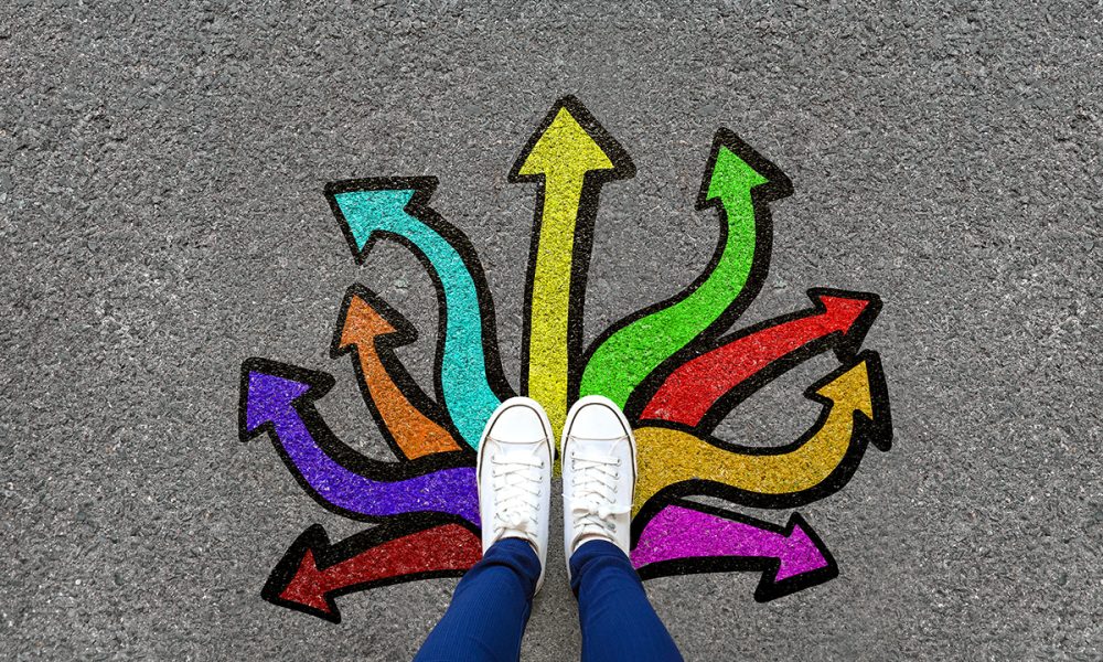 Feet and arrows on road background. Pair of foot standing on tarmac road with colorful graffiti arrow sign choices, creative and idea concept. Selfie woman wearing white shoe or sneaker. Top view.